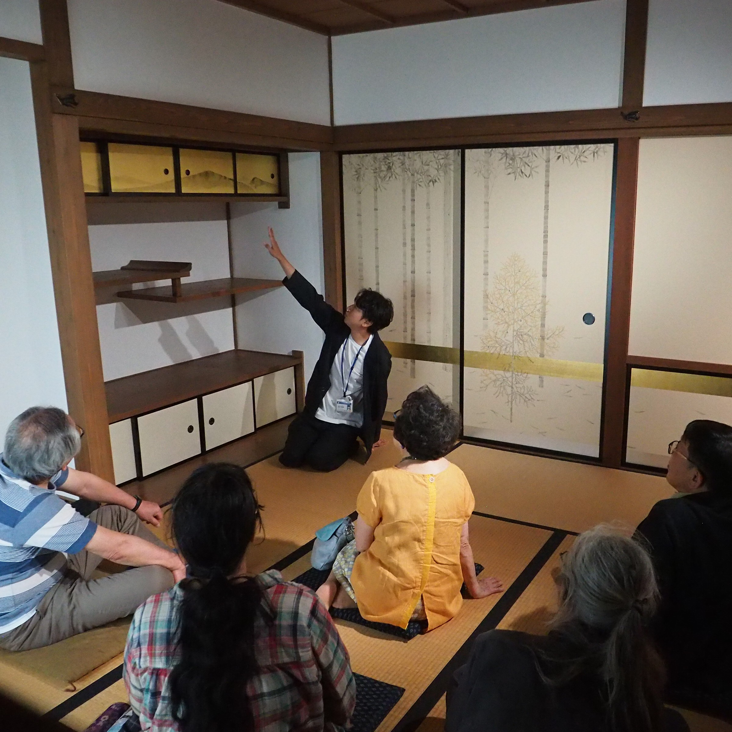 障壁画の説明をする人と聞く人たちの画像
